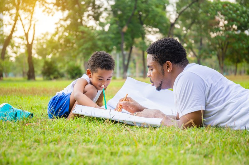 A father drawing with his son outside in the summer by the Law Offices of Robert E. O’Connor